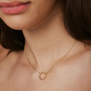 Close-up of a woman wearing a gold necklace with a circular snake pendant.