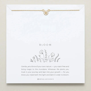Gold necklace with a gemed flower pendant on a card with floral design and text