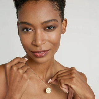 Woman wearing a gold necklace with a circular pendant against a neutral background