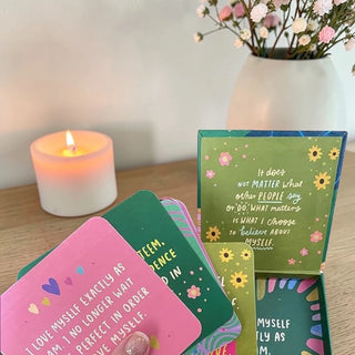 Motivational cards with inspirational quotes on a wooden surface with a candle and flowers in the background.