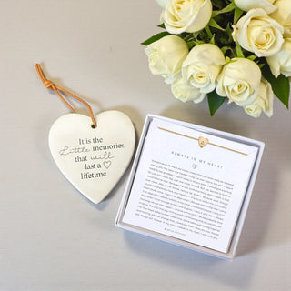 Heart-shaped plaque with engraved text, necklace in box, and white roses on a light background