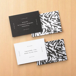Four black and white cards with motivational text on a wooden surface