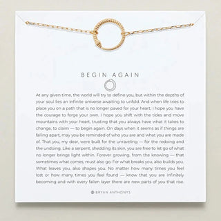 Gold necklace with a thin chain and a circular snake pendant in the middle on a card with text and branding
