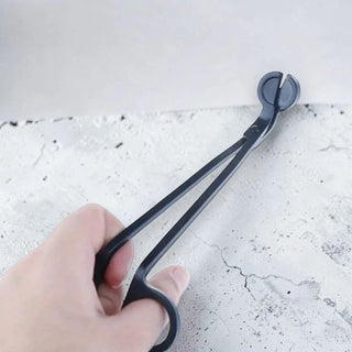 Black candle wick trimmer held by a hand on a light grey surface
