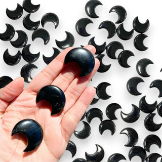 Black crescent-shaped obsidian crystals held in a hand with more black crystals in the background.