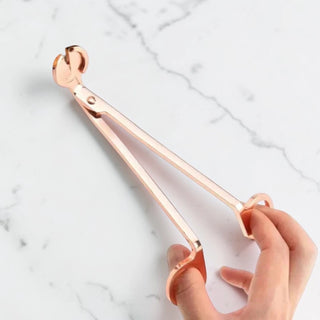 Rose gold candle wick trimmer held by a hand on a marble background