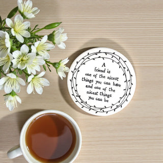 Coaster with a quote, cup of tea, and flowers on a wooden surface