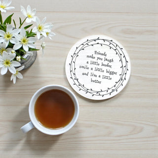 Coaster with a quote next to a cup of tea on a wooden surface with flowers.