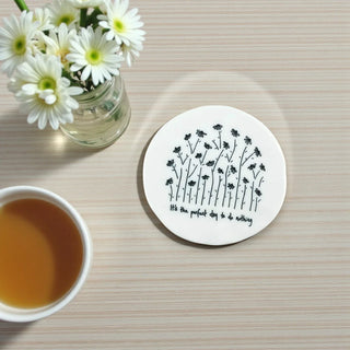 Coaster with floral design and text on a table with flowers and tea.