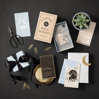 Collection of tarot cards, books, and decorative items on a dark surface with a plant and scissors.