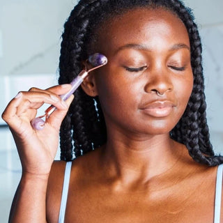 Woman applying a crystal roller to her face with a neutral background