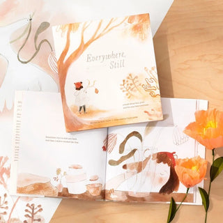 Open book with illustrations on a wooden surface with flowers.