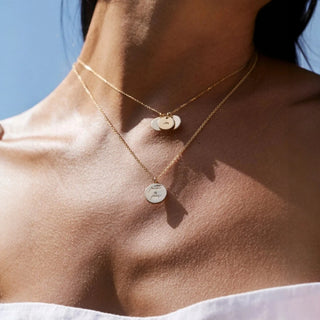 Close-up of a person wearing two gold necklaces with circular pendants.
