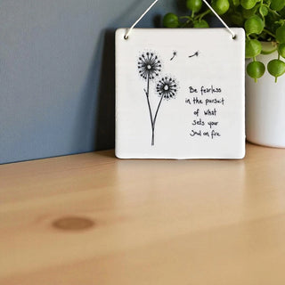 Decorative wall plaque with dandelion illustration and motivational quote on a wooden surface.