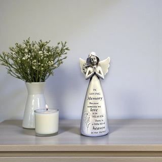 Silver resin angel statue with wings and hands in a prayer position on a wooden table with the inscription In loving memory because someone we love is in heaven there is a little bit of heaven in our home