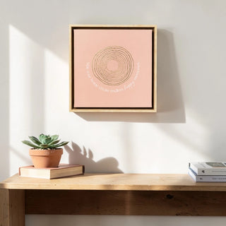 Framed artwork on a wall above a wooden desk with a plant and books.