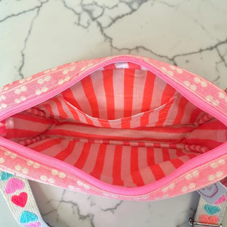 Pink and red striped bag interior with a heart-patterned strap on a marble surface