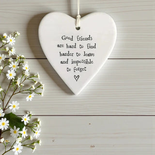 White heart-shaped plaque with a quote on a wooden surface with flowers