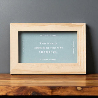 Framed print with a quote by Charles Dickens on a wooden surface and gray wall background