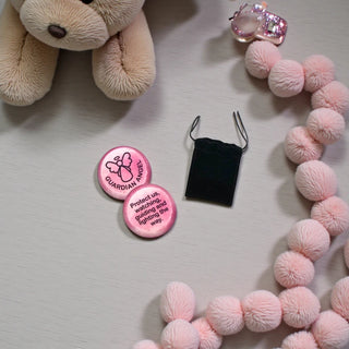 Pink worry stone with 'Guardian Angel' text, a plush toy, and pink pom-pom decorations on a light surface.