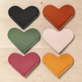 Set of six heart-shaped leather-look page holders in different colours on a wooden surface