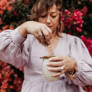 Woman in a light purple dress holding a small ceramic cup with flowers in the background.