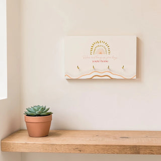 Wooden wall hanging with 4 metal hooks for keys and a decorative quote about home with a potted succulent on a wooden shelf in the background