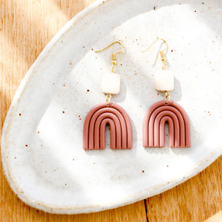 Pink arch-shaped earrings on a white speckled dish with a wooden background