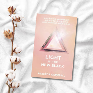 Book titled 'Light is the New Black' by Rebecca Campbell on a textured white surface with cotton and branches.
