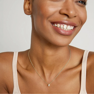 Woman wearing a gold necklace with a small pendant on a plain background