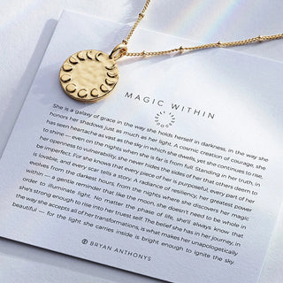Gold necklace with a circular pendant on a piece of paper with text