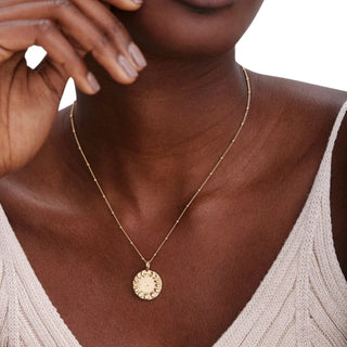 Woman wearing a gold necklace with a circular pendant on a neutral background