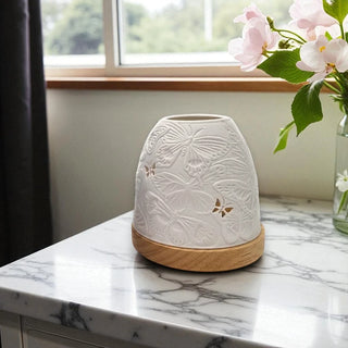 White porcelain tea light holder with a butterfly relief pattern with wooden base on a marble surface, flowers in the background