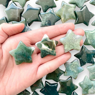 Hand holding green star-shaped Moss agate crystal stones with more moss agate stones in the background