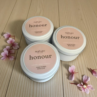 Three 'nurture honour' candles on a wooden surface with pink flowers.