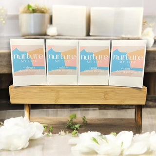 Four 'nurture MY LIFE' shower steamers on a wooden stand with flowers in the foreground.