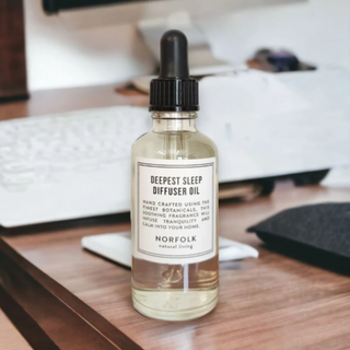 Bottle of 'Deepest Sleep Diffuser Oil' by Norfolk on a wooden surface with a blurred background.