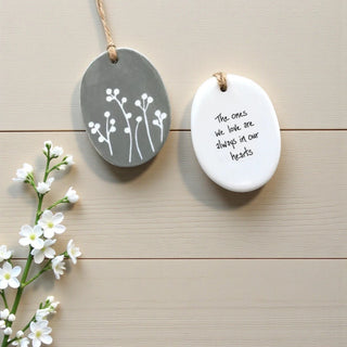 Two ceramic ornaments with floral design and text on a wooden surface with flowers.