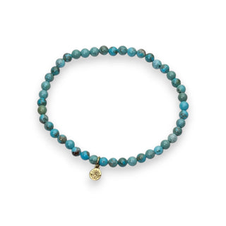 Turquoise beaded bracelet with a gold lotus charm on a white background