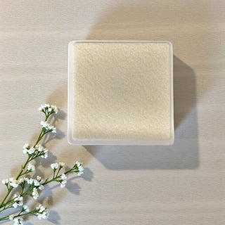 Back of the Square coaster on a textured surface with a sprig of white flowers.