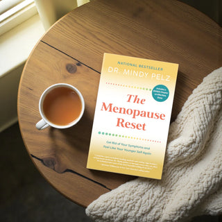 Book titled 'The Menopause Reset' by Dr. Mindy Pelz on a wooden table with a cup of tea.