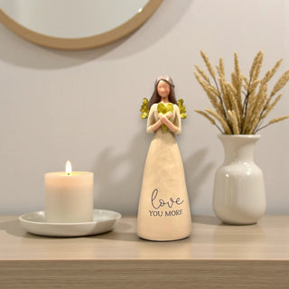 A resin angel holding a gold heart with the inscription Love You More