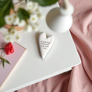 Heart-shaped ceramic ornament with text on a white surface with flowers and a pink fabric background