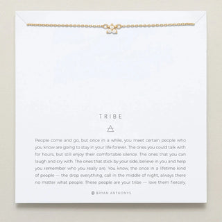 Gold necklace on a card with text about 'tribe' by Bryan Anthony on a beige background