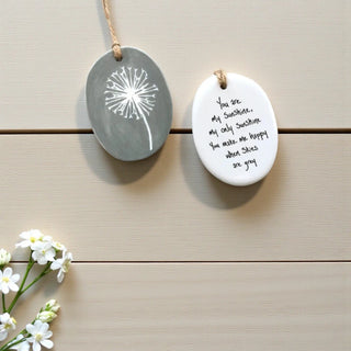 Two ceramic plaques with a dandelion design and text on a wooden surface.