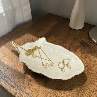 White Feather shaped Jewellery dish with gold border holding necklaces and earrings on a wooden surface